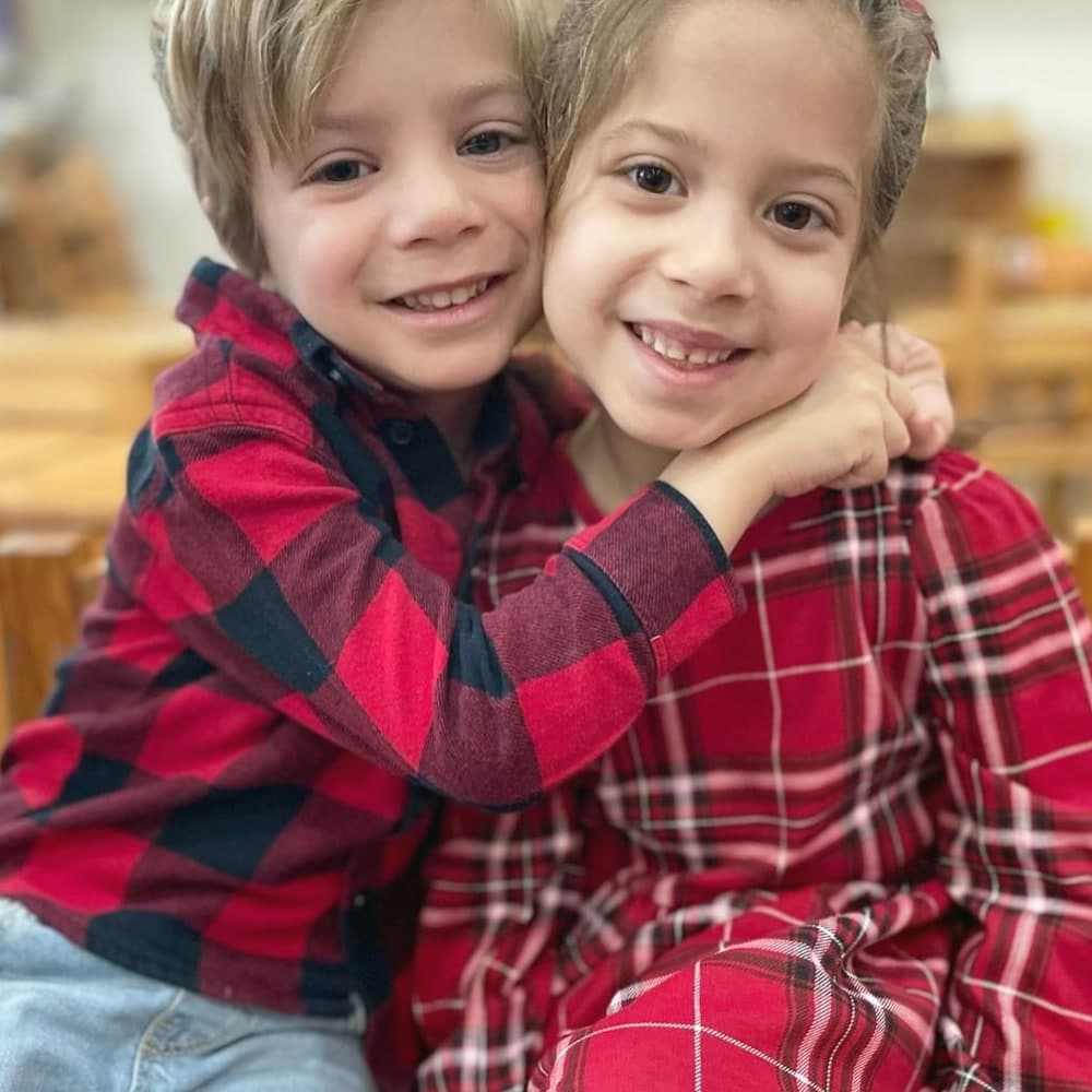 Dos niños abrazados sonriendo a la cámara en el salón