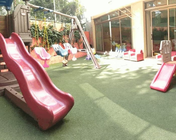 Jardín del kínder con resbaladilla y columpios sobre pasto