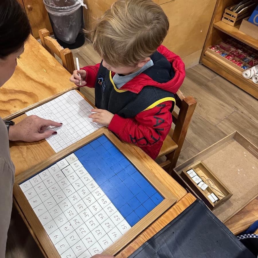 Niño escribiendo los números del tablero del cien junto a su guía