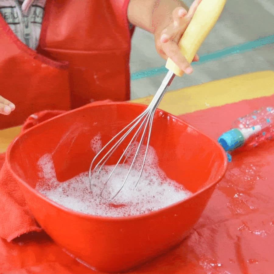 Niña batiendo con un globo en la mesa de vida práctica